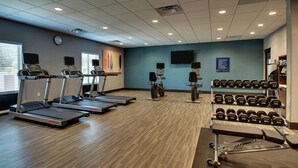 Un gimnasio con cintas de correr, elípticas, una banca y un estante con mancuernas.