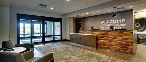 A reception area with a wooden reception desk, a seating area with chairs and a table, and a large window with a view of the outside.