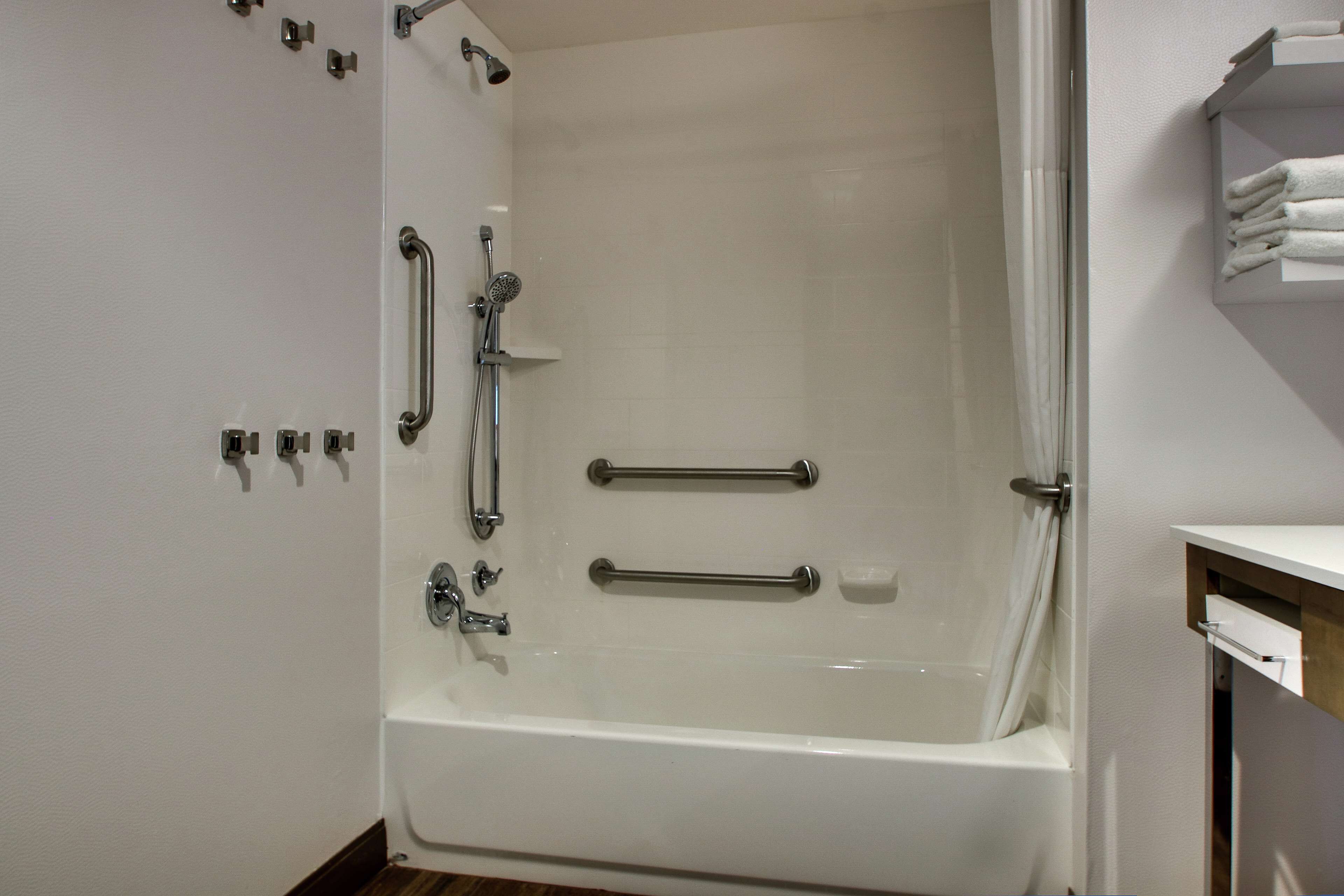 A modern bathroom with a bathtub, grab bars, and a towel rack.