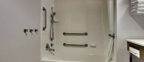 A modern bathroom with a bathtub, grab bars, and a towel rack.