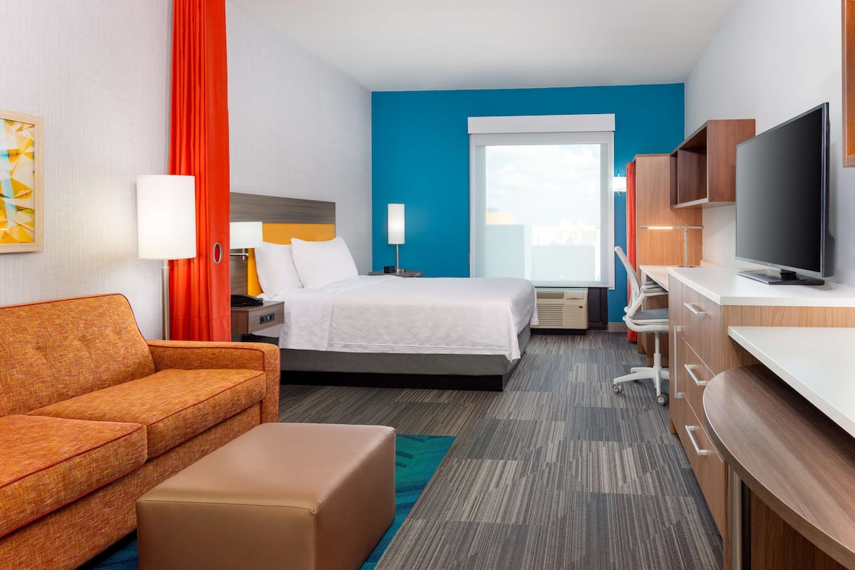 A hotel room with a bed, a sofa, a desk, a television, and a window.