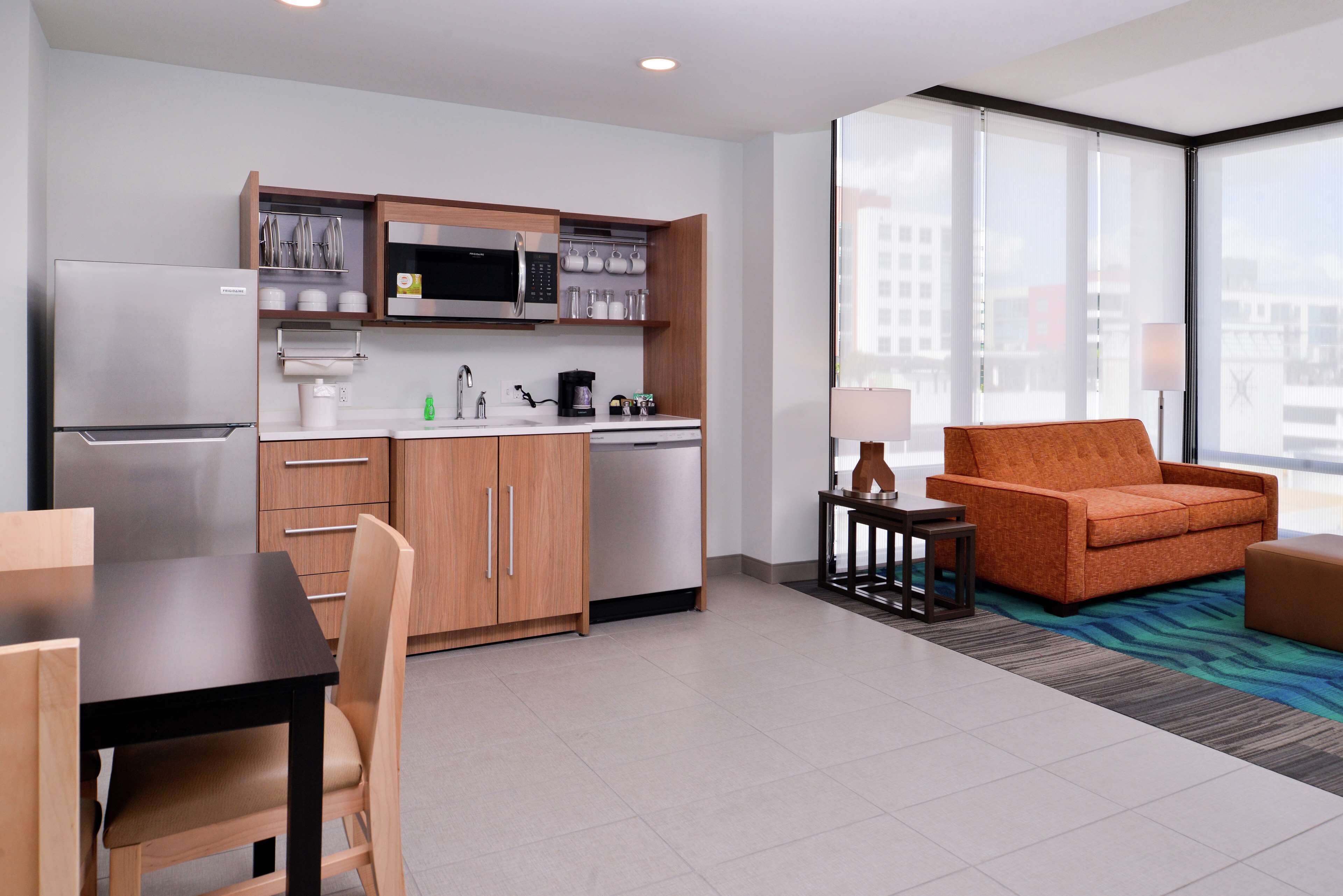 A modern hotel room with a kitchenette, a dining area, and a seating area with a view.