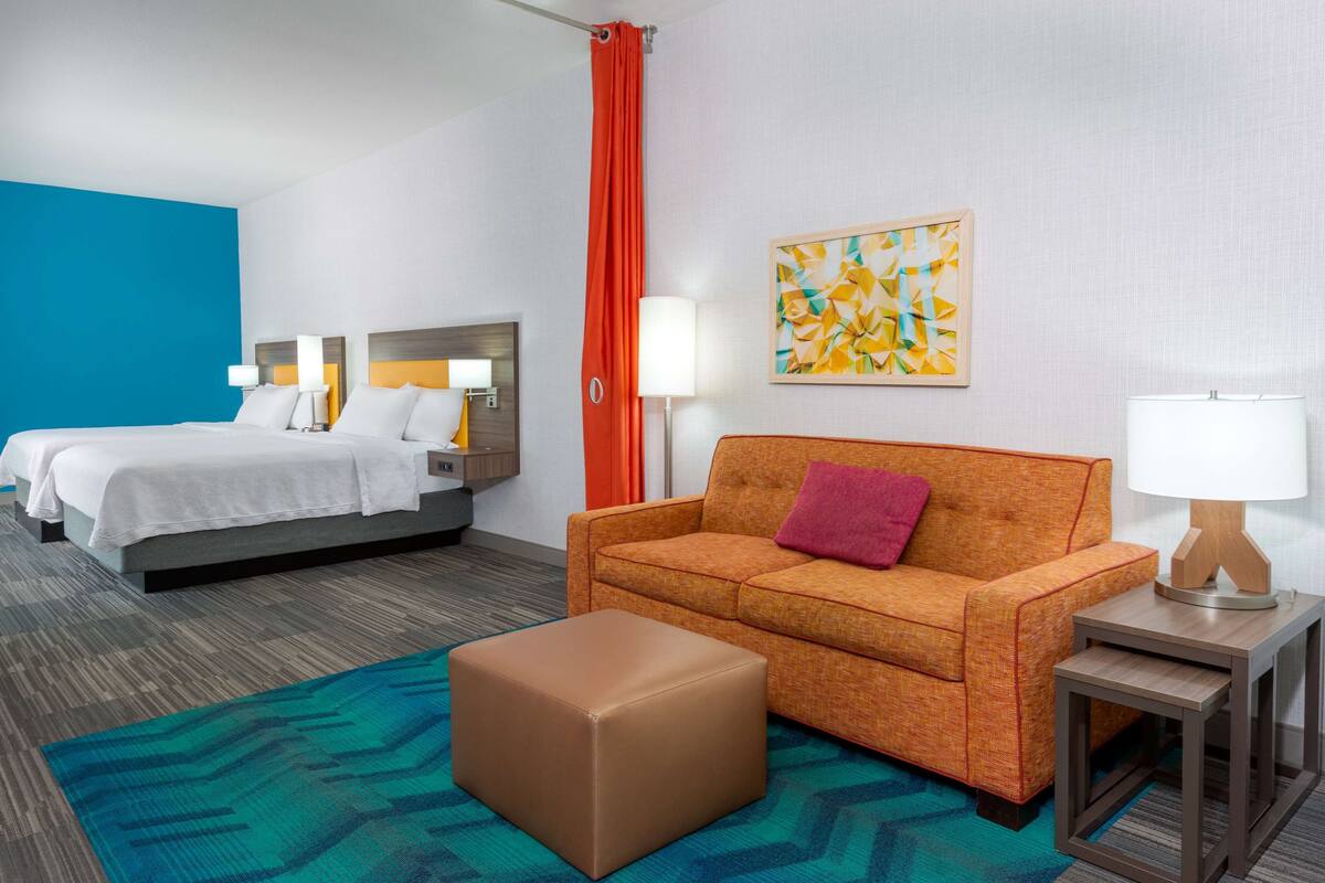 A hotel room with a bed, a sofa, a small table, and a rug.