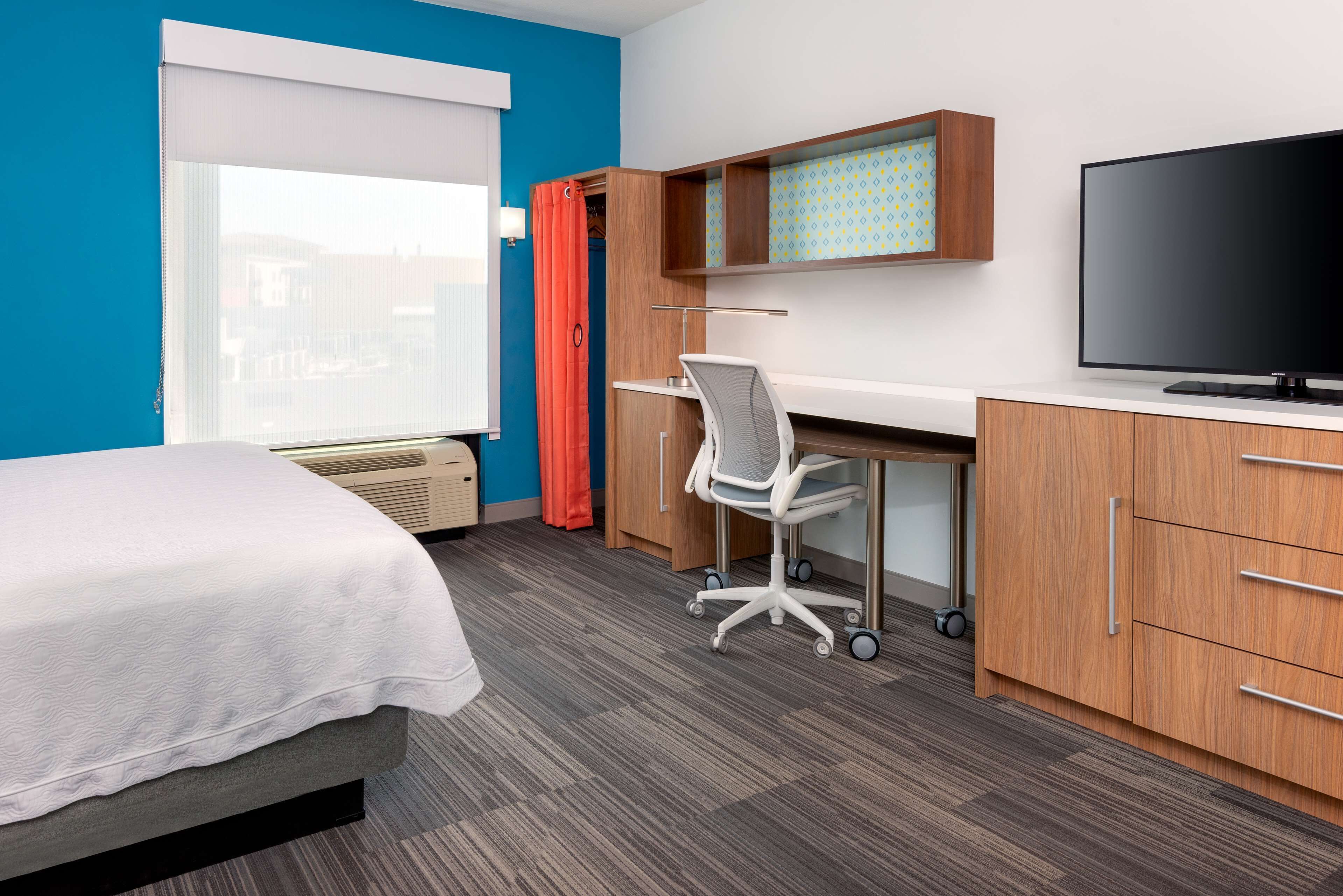 A hotel room with a bed, desk, chair, television, and a window with curtains.