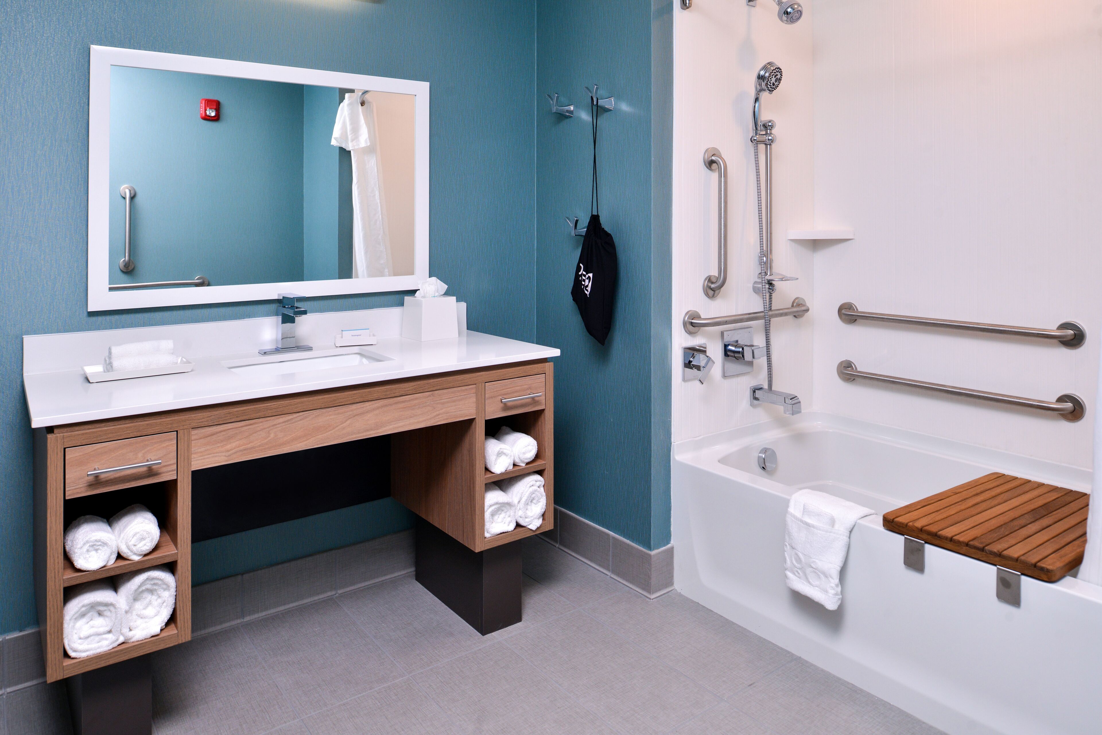 A modern bathroom with a white sink, wooden vanity, and a bathtub with grab bars.