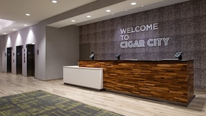A reception desk with a "WELCOME TO CIGAR CITY" sign, a modern design with a wooden panel and a white counter.