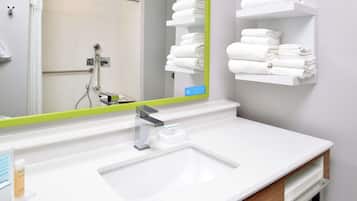 Une salle de bain moderne avec un lavabo blanc, un miroir à cadre vert et des étagères où sont soigneusement pliées des serviettes blanches.
