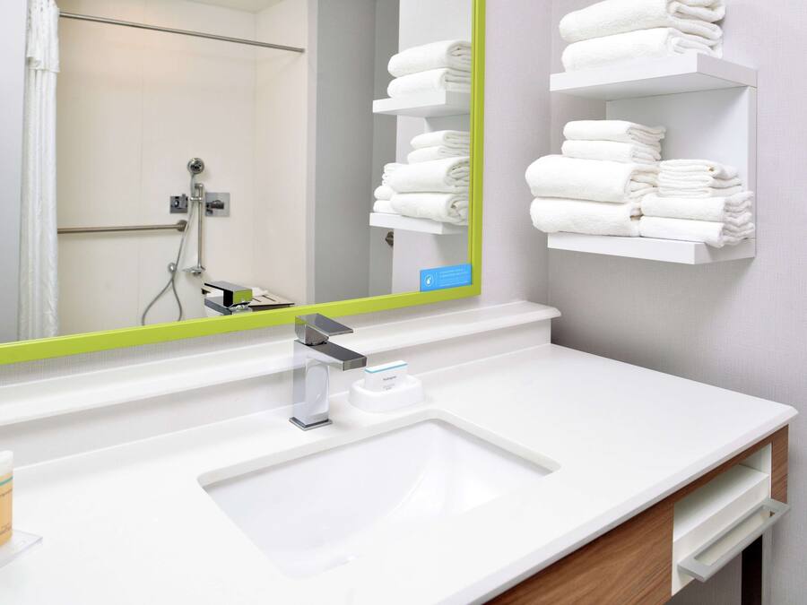 Une salle de bain moderne avec un lavabo blanc, un miroir à cadre vert et des étagères où sont soigneusement pliées des serviettes blanches.