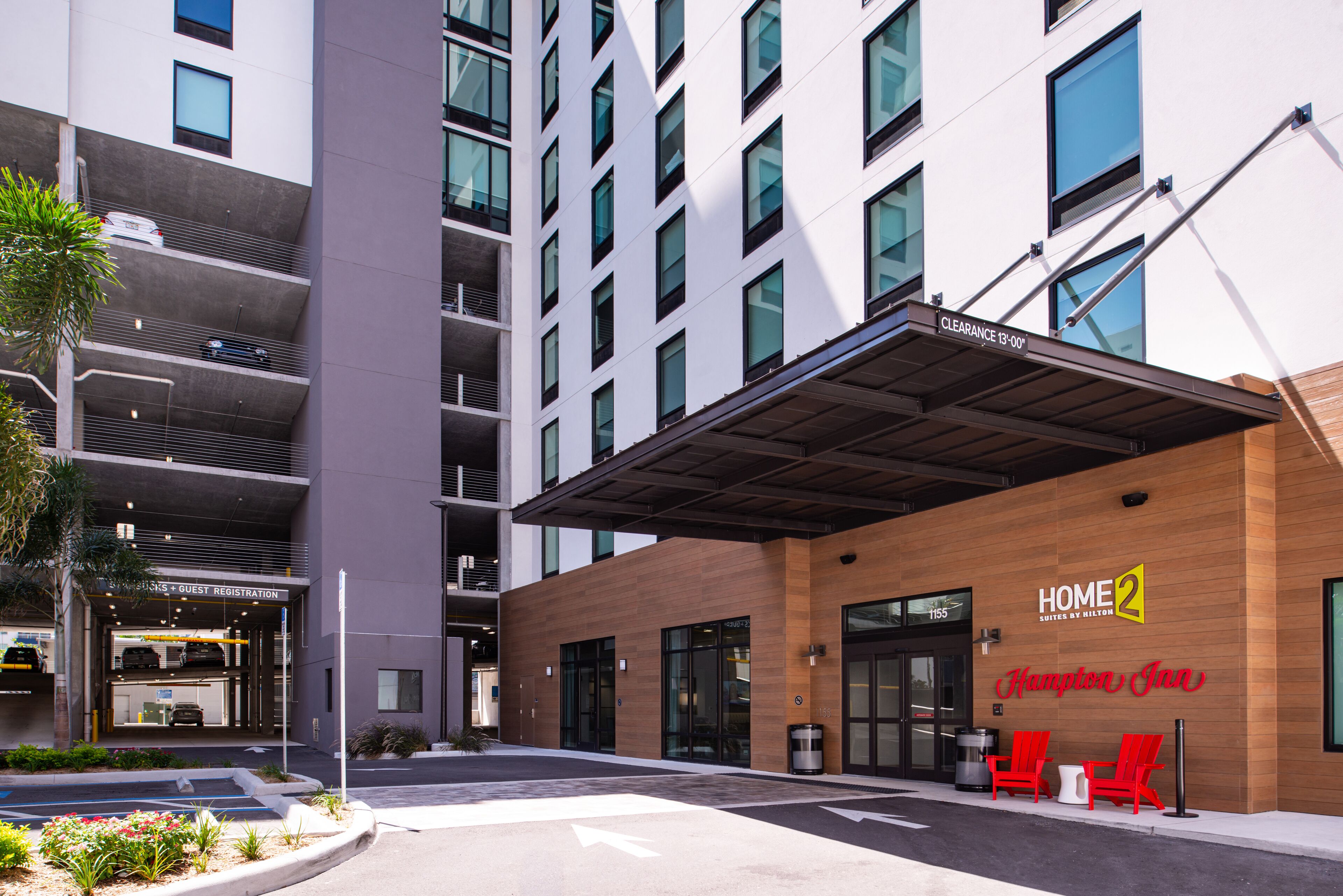 A modern hotel entrance with a covered waiting area, guest registration, and a clear sign indicating a 13-00 clearance.