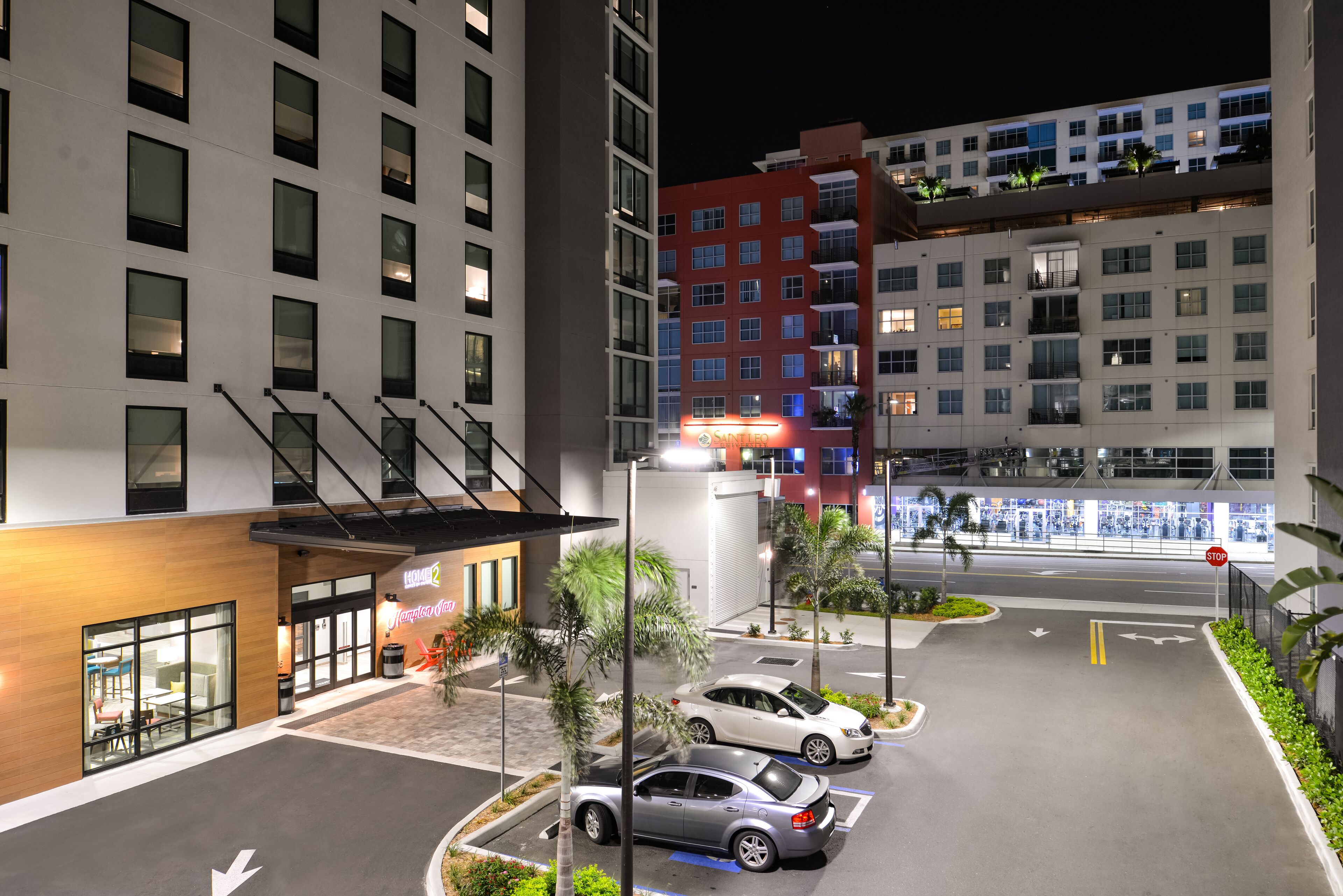 Um estacionamento de hotel com vários carros, uma placa de pare e um edifício com vários andares e varandas.
