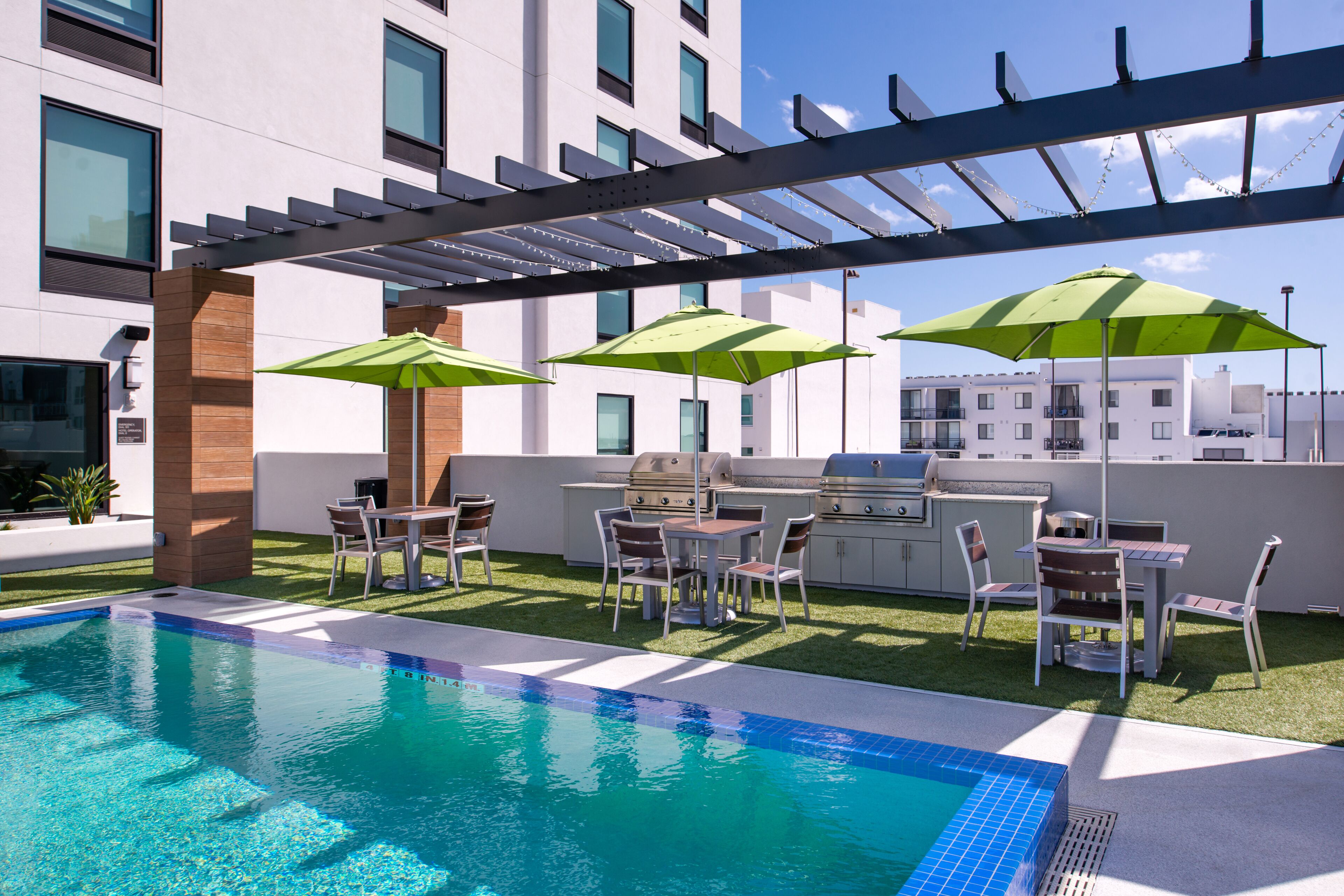 Un área de piscina en la azotea con una zona de barbacoa, asientos exteriores y sombrillas.