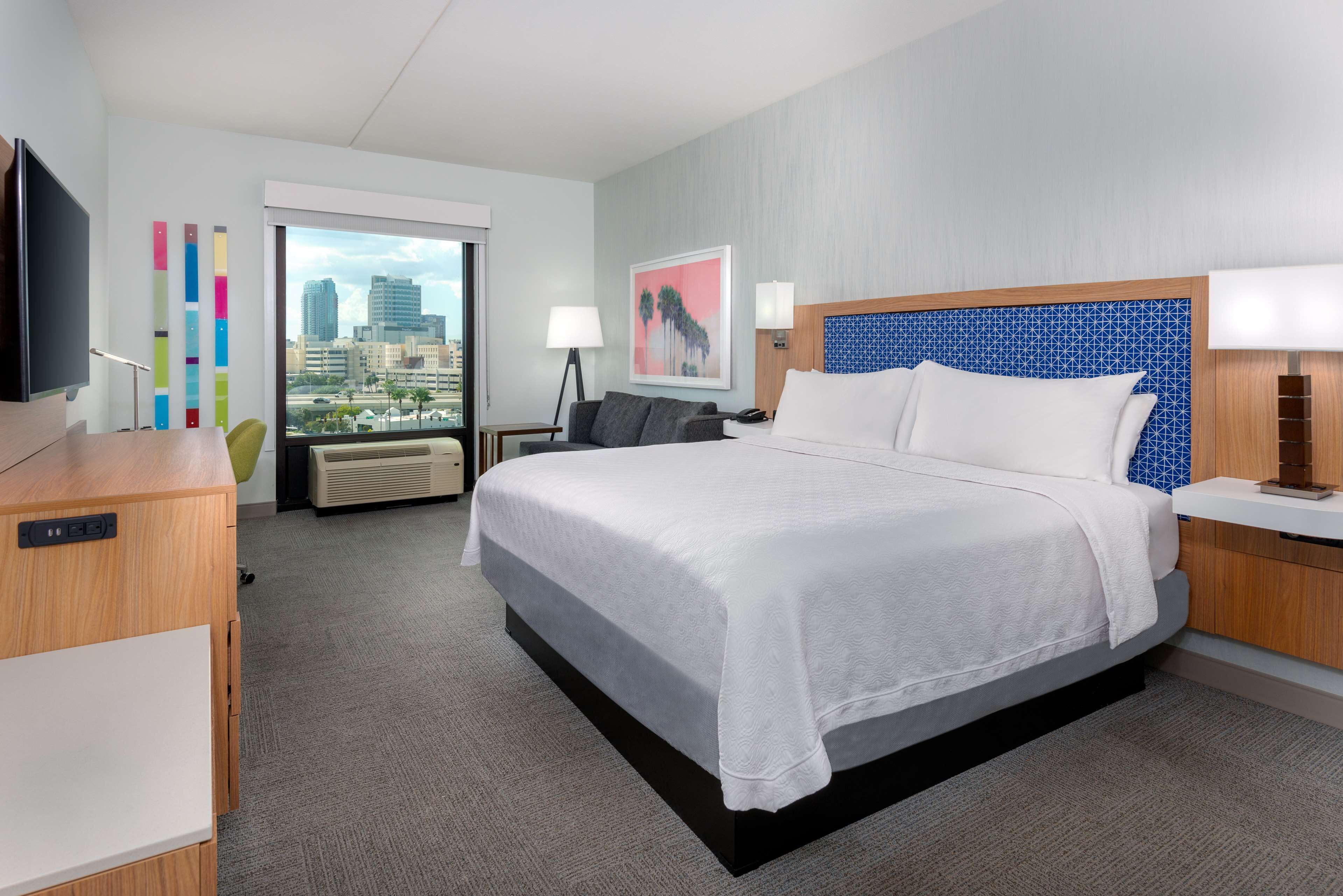 Hotelkamer met een groot bed, een bureau, een stoel, een televisie, een raam met uitzicht op de stad en een schilderij aan de muur.