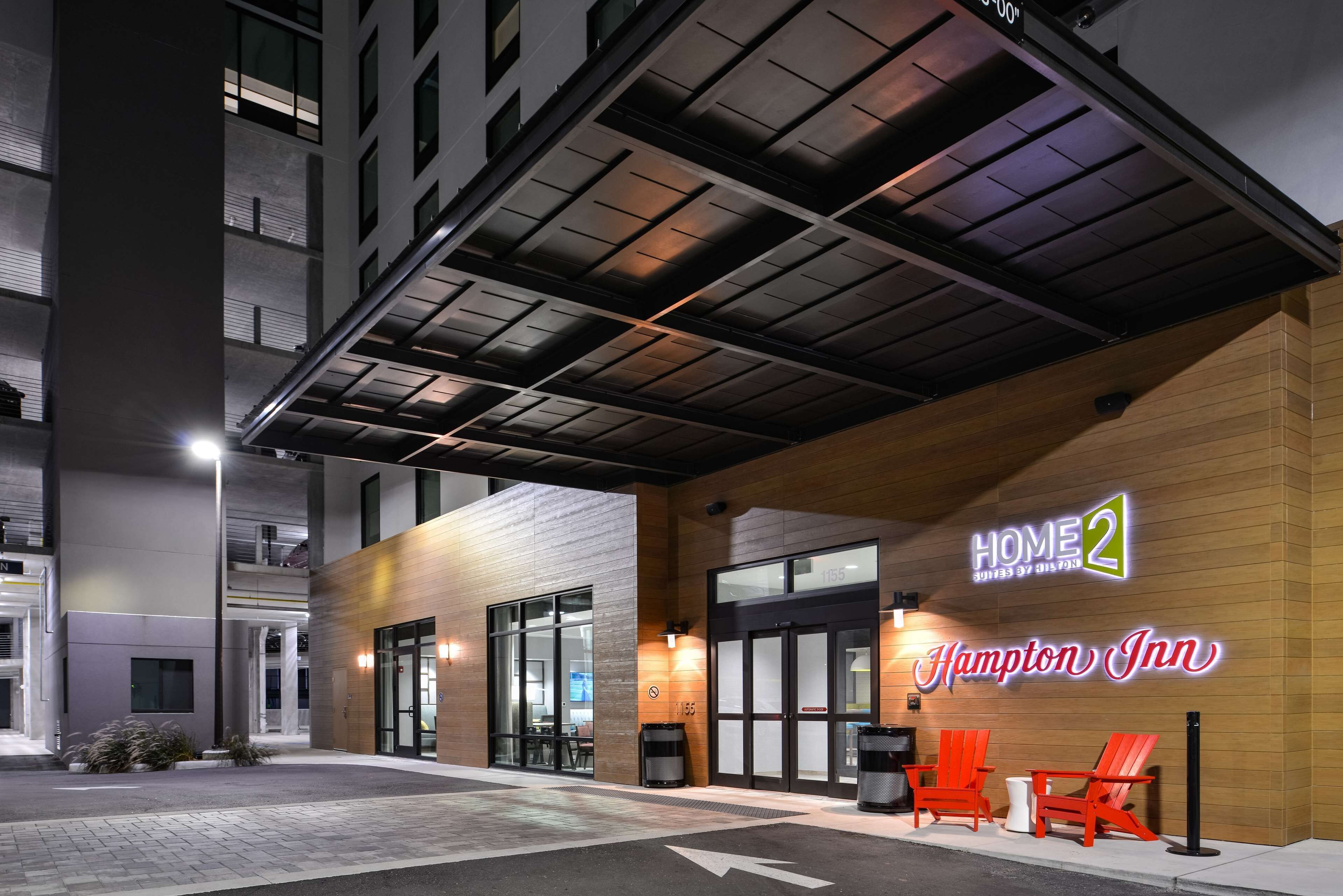 A Hampton Inn hotel entrance with a modern design, including a covered walkway and a sign for the Hampton Inn Hampton.