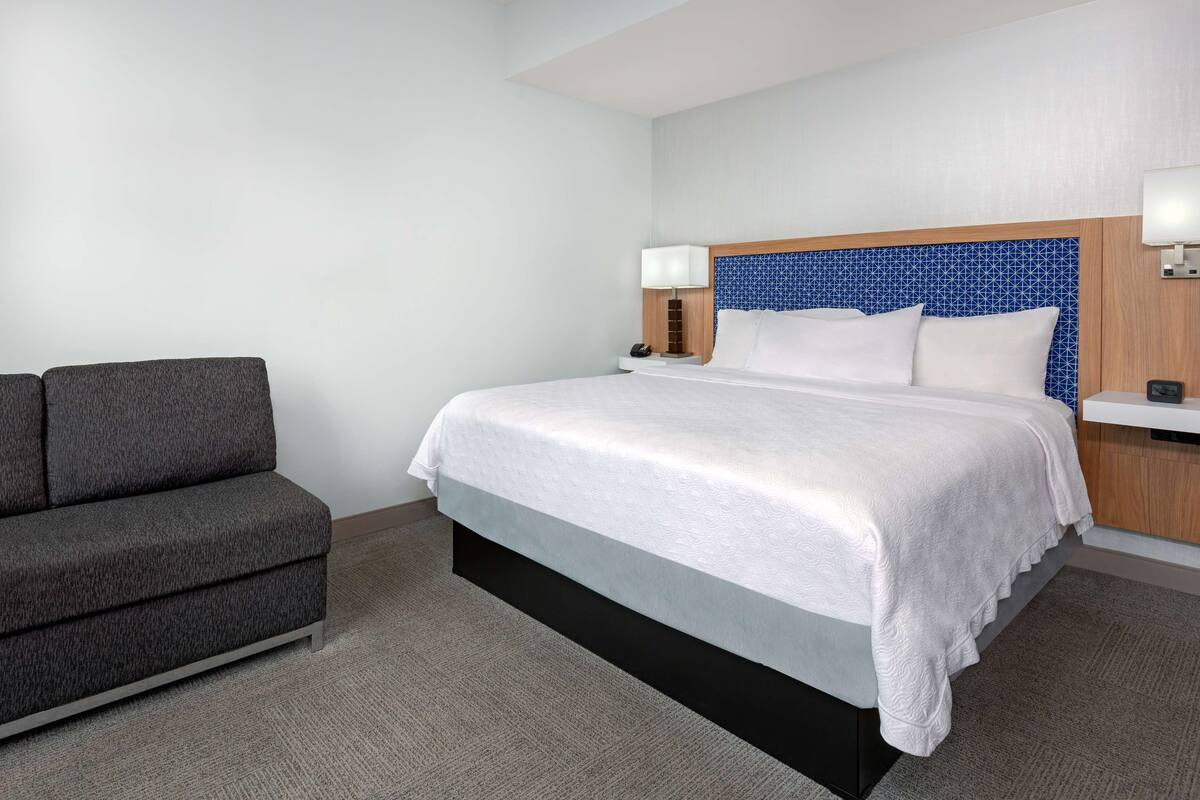 A hotel room with a bed, a sofa, a nightstand, and a lamp.