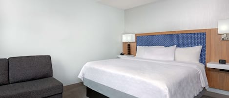 A hotel room with a bed, a sofa, a nightstand, and a lamp.