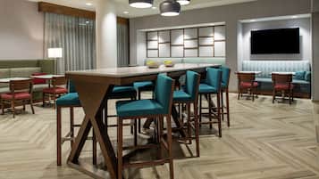 Un moderno vestíbulo de hotel con una larga mesa de comedor, varios taburetes de bar, un sofá y un televisor montado en la pared.