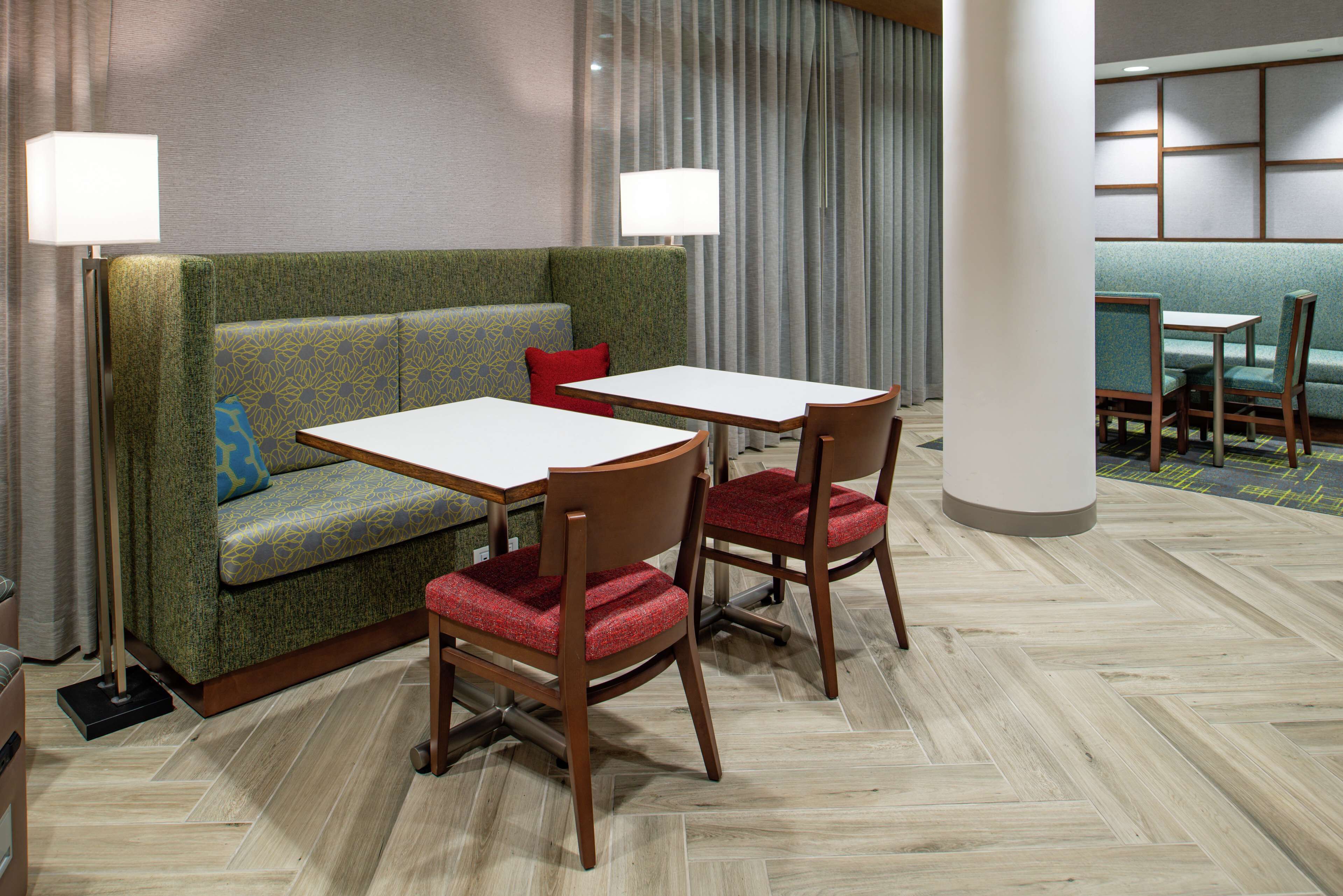 Ein Hotelzimmer mit einem grünen gemusterten Sofa, zwei Holzstühlen, einem weißen Tisch und einer Lampe.
