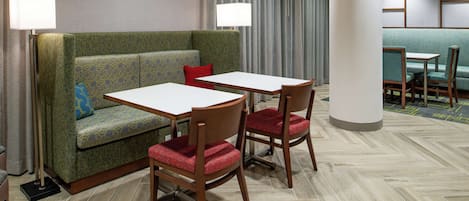 Ein Hotelzimmer mit einem grünen gemusterten Sofa, zwei Holzstühlen, einem weißen Tisch und einer Lampe.