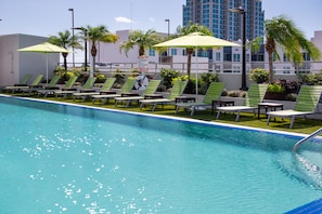 A poolside area with lounge chairs and umbrellas, a clear pool, and a cityscape in the background.