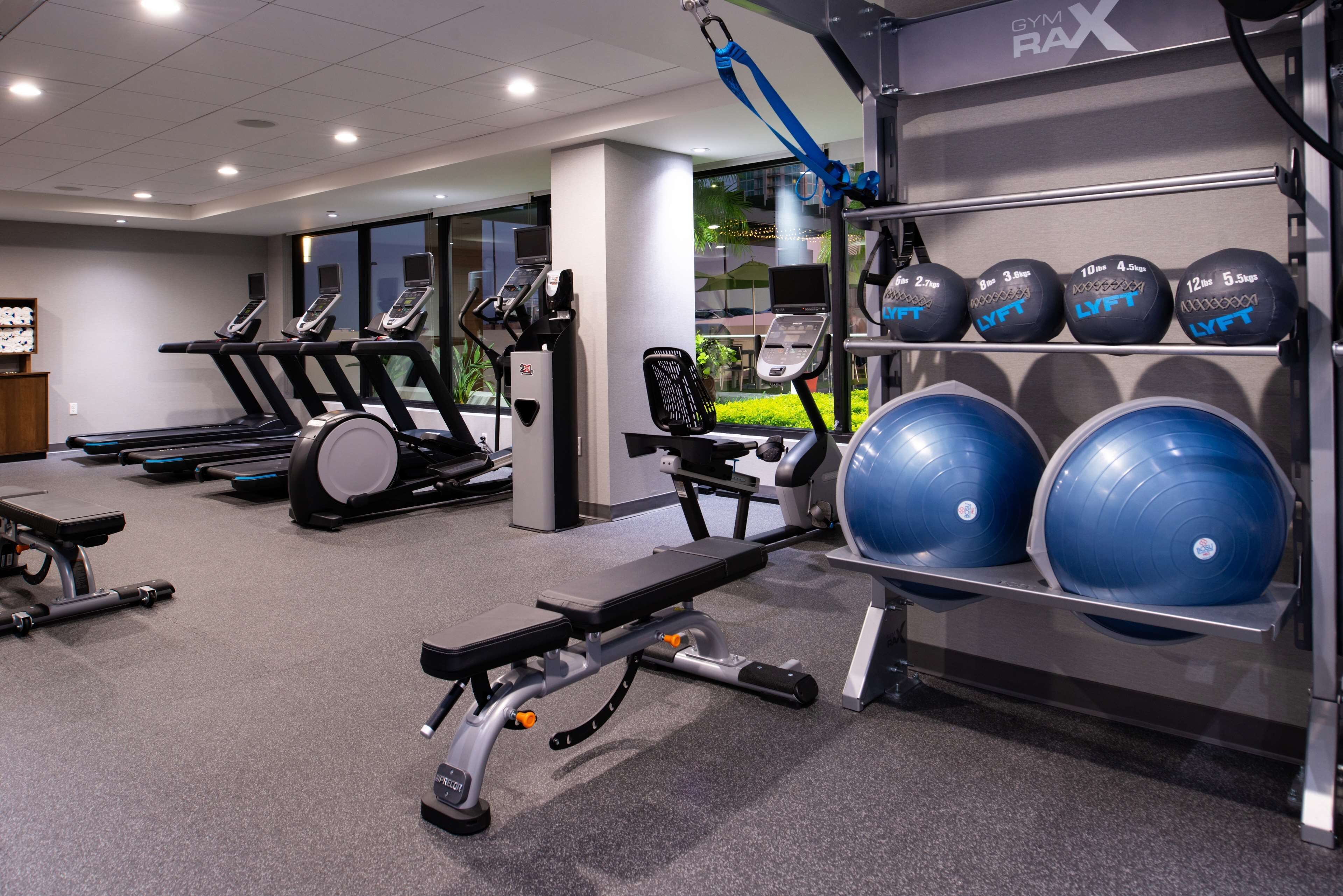 Ett gym med löpband, en bänkpress och ett ställ med blåa medicinbollar.