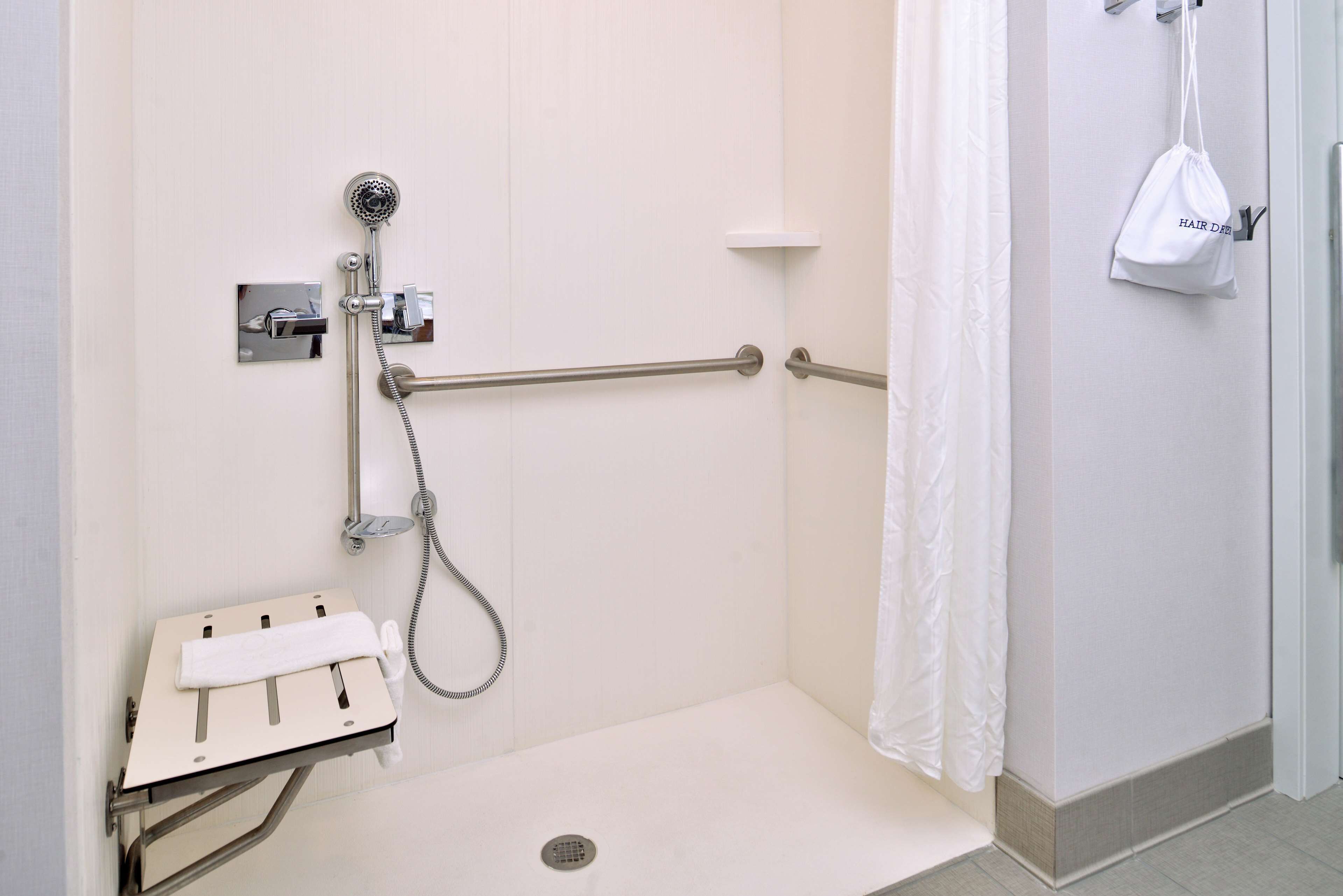 Un espace douche équipé d’une barre d’appui, d’un pommeau de douche à main et d’un sac blanc accroché au mur.