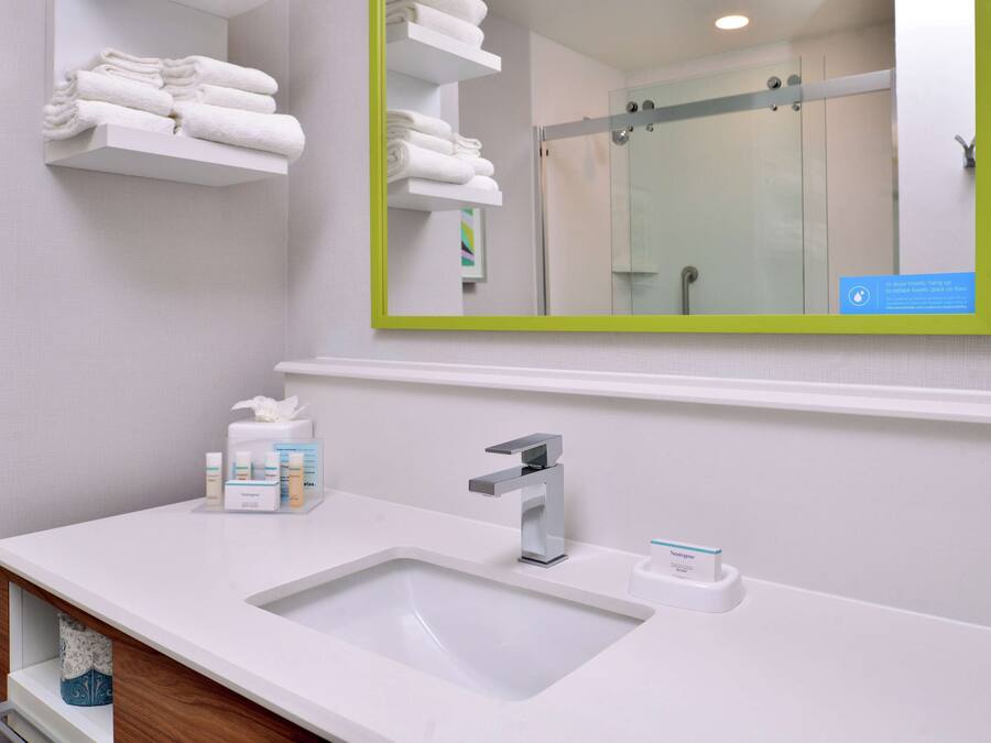 A modern bathroom with a white sink, a mirror with a green frame, and shelves with folded towels.