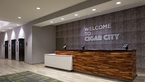 Un espace d’accueil avec une pancarte indiquant « BIENVENUE À CIGAR CITY », un comptoir de réception et plusieurs ascenseurs.