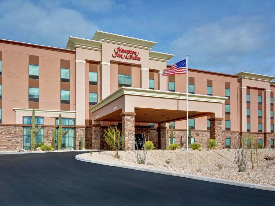 A Hampton Inn & Suites hotel with a modern facade, large windows, and a covered entrance area.