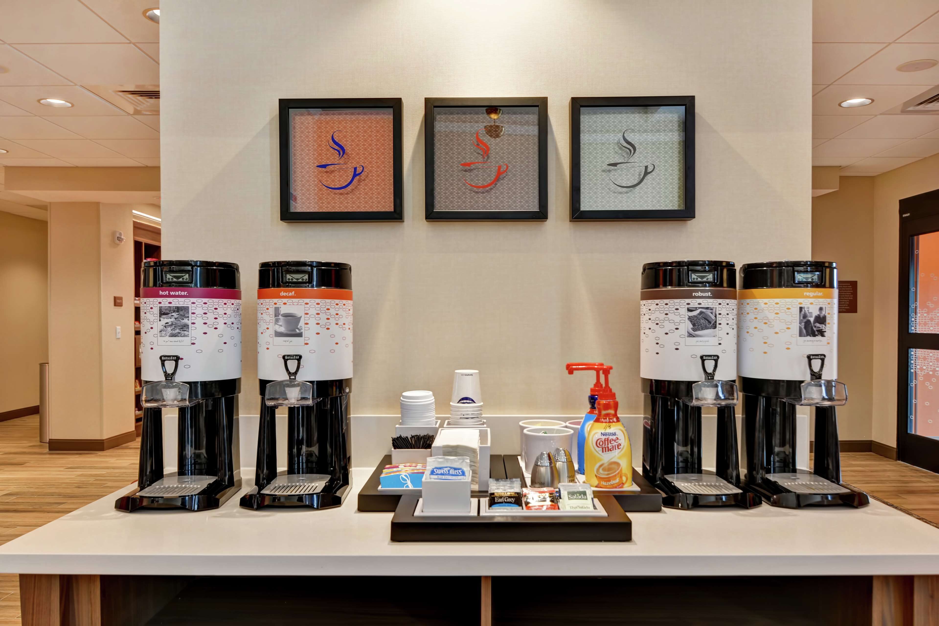 A coffee station with multiple coffee machines and a selection of coffee pods and creamer bottles.