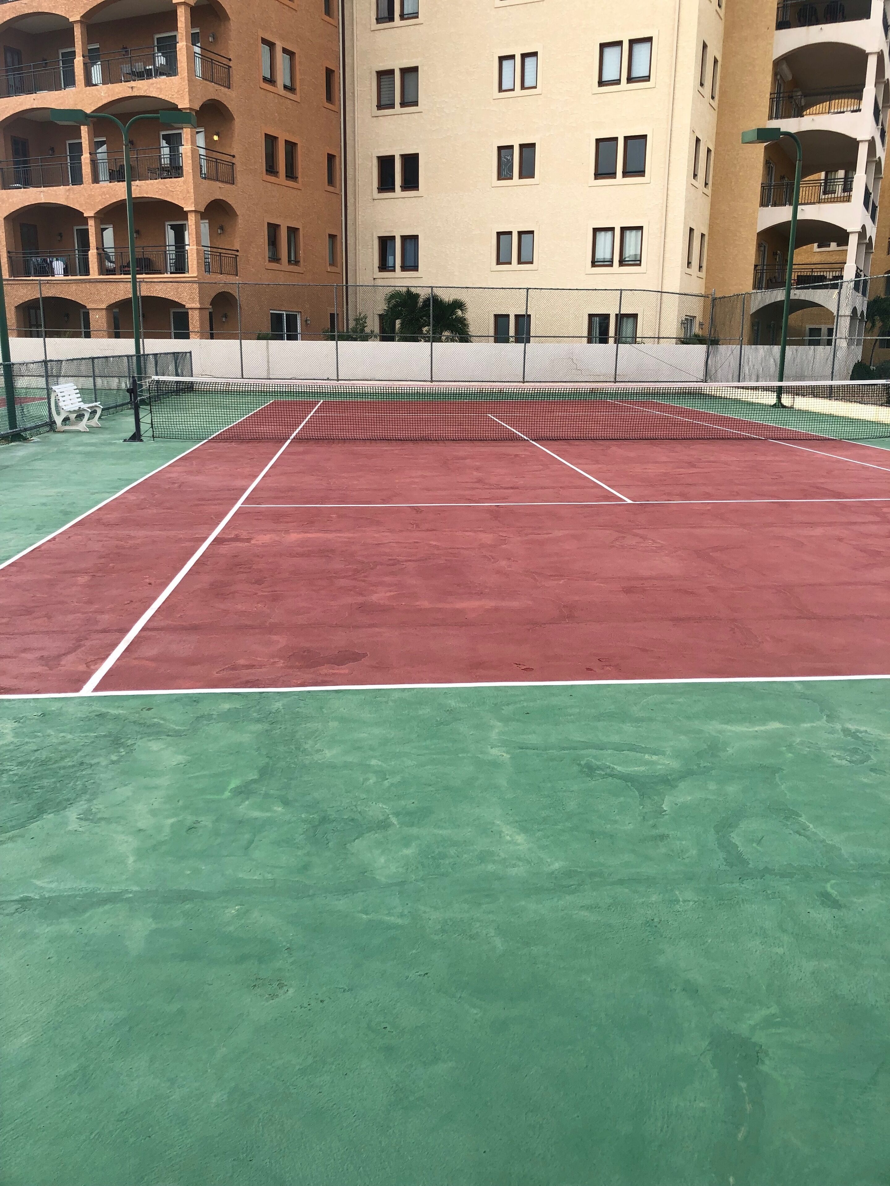 Una cancha de tenis con una red, rodeada por una valla.