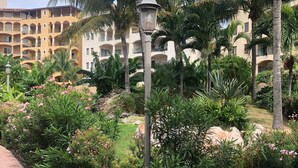Un jardin aménagé avec des palmiers, un chemin pavé et, au fond, un bâtiment doté de nombreux balcons.