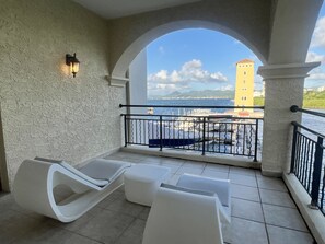 Ein Balkon mit weißen Lounge-Stühlen und Blick auf das Meer sowie ein gelbes Gebäude.