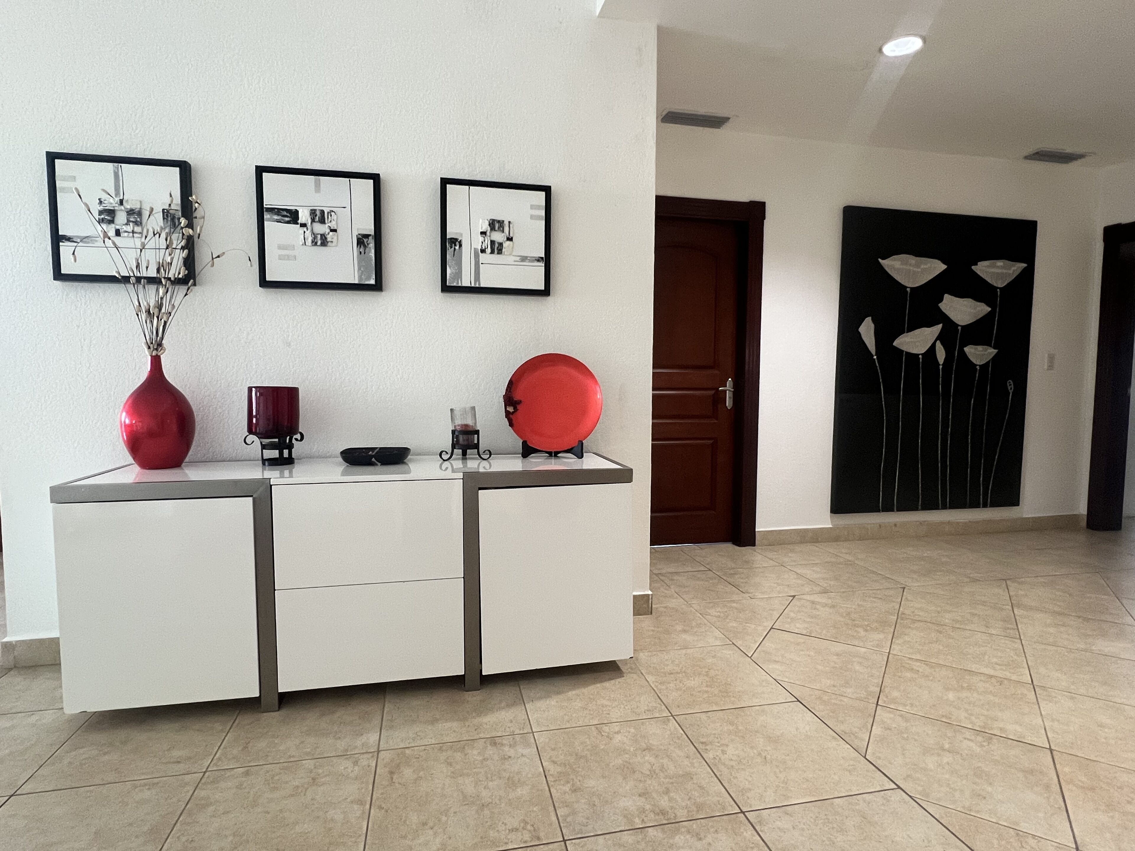 A reception area with a white console table, a red vase, and three framed pictures on the wall.