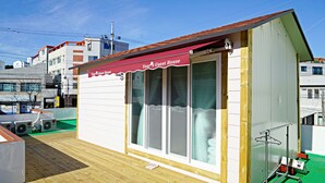 A small guest house with a red awning, large windows, and a wooden deck. - Yours Guesthouse (Tongyeong)