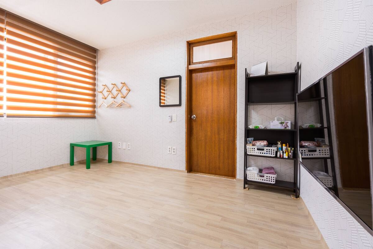 Ein Zimmer mit Holztür, einer grünen Bank, einem an der Wand befestigten Spiegel und einem Regal mit Körben.