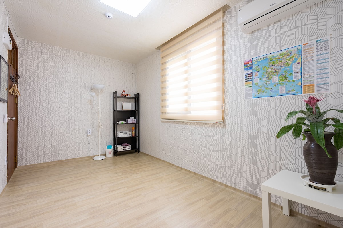 Ein Zimmer mit Holzboden, einer schwarzen Regaleinrichtung, einem weißen Tisch mit einer Vase und einem Fenster mit Jalousien.