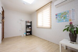 A room with a wooden floor, a black shelving unit, a white table with a vase, and a window with blinds. - Yours Guesthouse (Tongyeong)