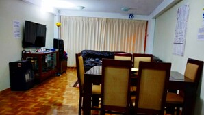 Una sala de estar con una mesa de comedor, sillas, un sofá, un televisor y un altavoz.