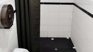 Un baño pequeño y estrecho con inodoro, zona de ducha y dispensador de papel higiénico.