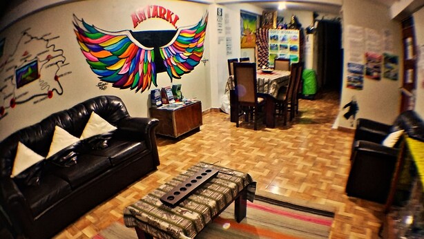 Una sala de estar con un sofá de cuero negro, un reposapiés estampado y un mural en la pared.