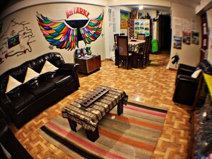 A living room with a black leather sofa, a patterned ottoman, and a wall mural. - Antarki Guest House (Cusco)