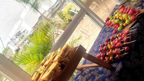 Un bufé de desayuno con sándwiches, brochetas de fruta y un vaso de jugo de naranja.