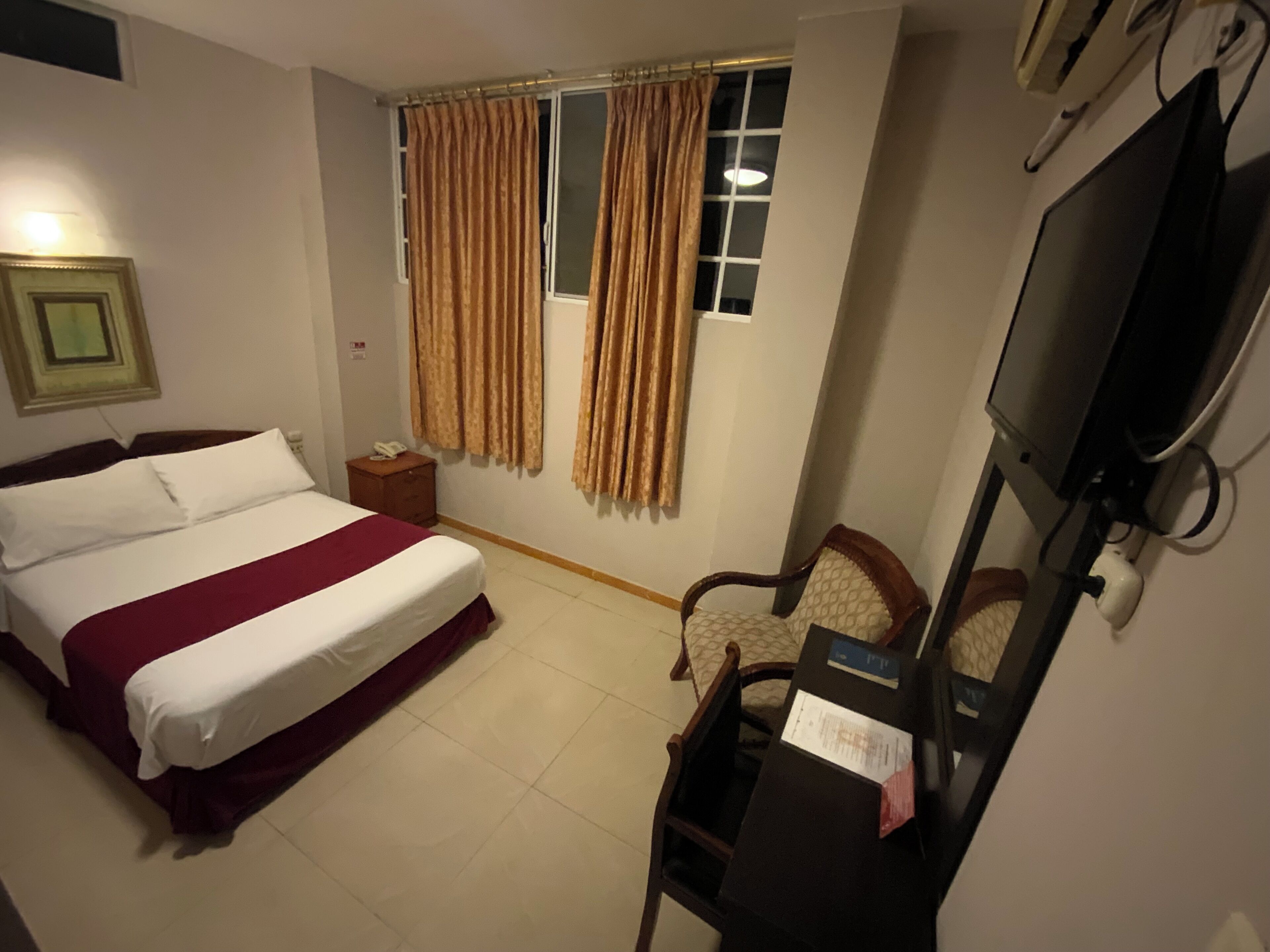 Habitación de hotel con una cama individual, un escritorio con silla, un televisor y cortinas en la ventana.