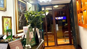 Zona de recepción de un hotel con un mostrador de mármol, obras de arte enmarcadas, una lámpara de araña e indicación de horarios de registro.