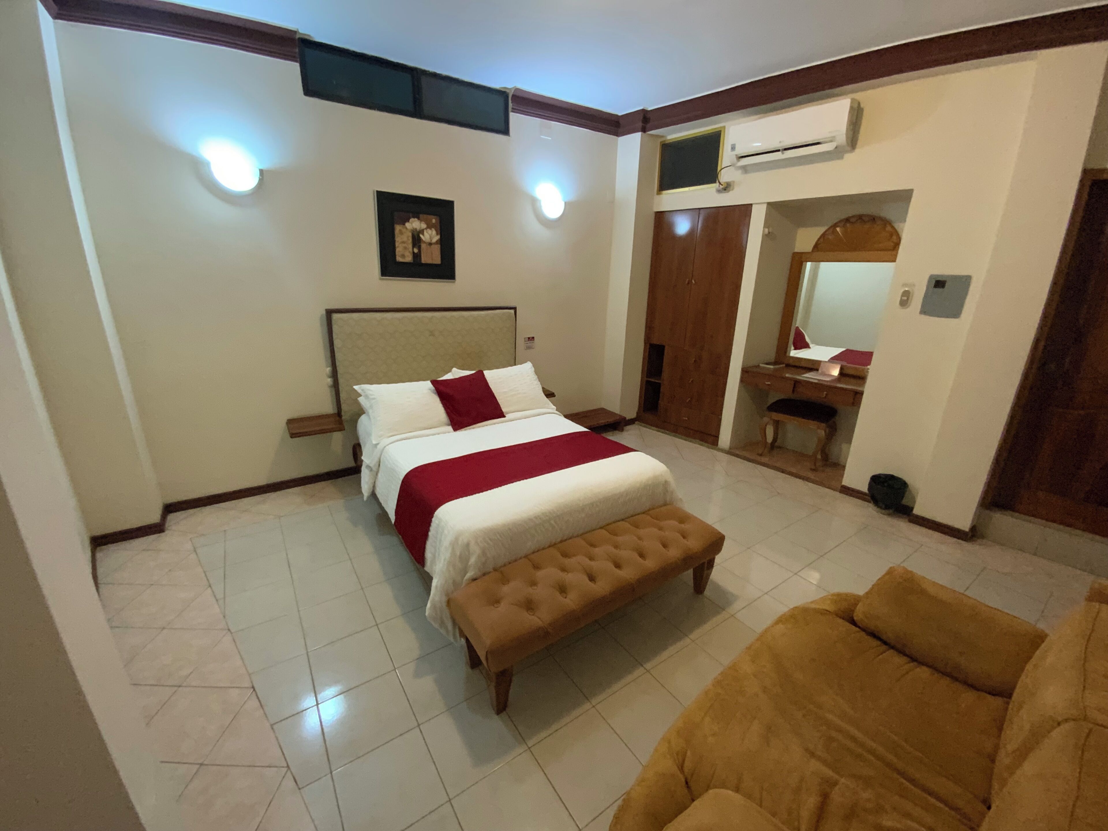 A hotel room with a bed, a bench, a desk, and a mirror.
