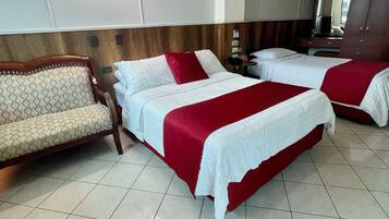 A hotel room with two beds, a sofa, a wooden headboard, and a tiled floor.