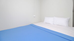 A single bed with a blue bedspread and two white pillows in a room with white walls and a white ceiling. - Kamar Keluarga Bandara IV Syariah (Tangerang)
