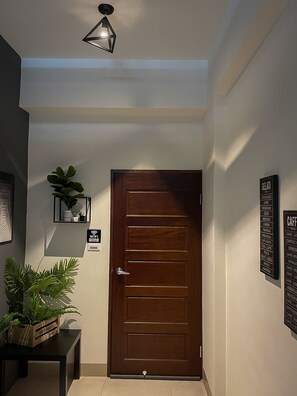 A hallway with a wooden door, a Wi-Fi sign, a potted plant, and a wall-mounted menu board listing coffee options. - Eddie's House (Ruisui)