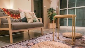 A living room with a sofa, cushions, a woven pouf, a small table, and a patterned rug. - Eddie's House (Ruisui)