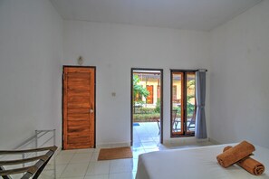 A hotel room with a bed, a wooden door, and an open door leading to an outdoor area with a table and chairs.